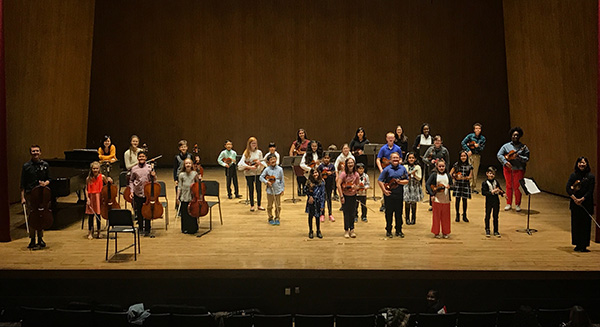 Photograph of String Project students of various grades and backgrounds standing on the Singletary center stage after a year-end performance.