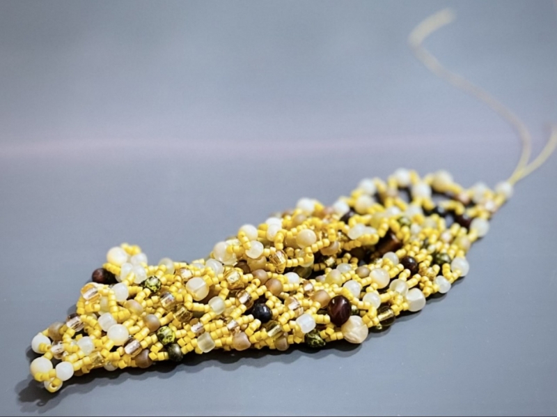 A sculptural piece using golden thread and yellow, pearl, and various stone-like beads.