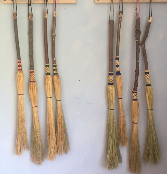 An assortment of rustic cobweb brooms hanging from wall pegs.