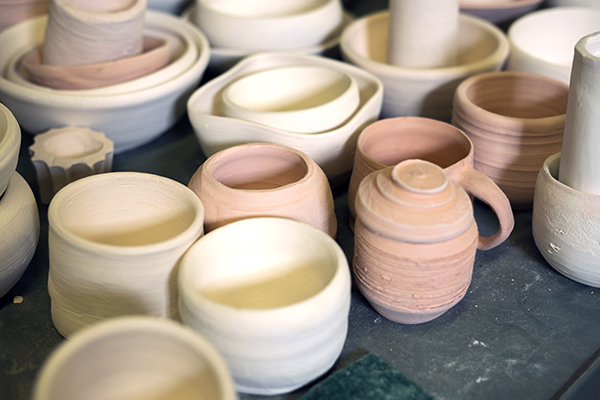 A variety of bone dry, bisque fired, and raw glazed pots on a table.