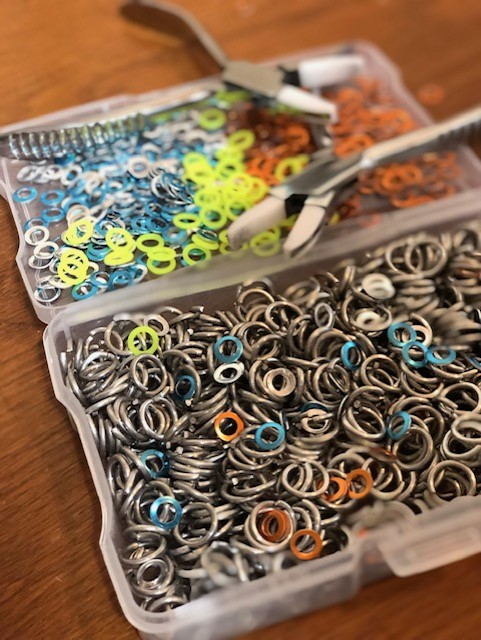 A storage box full of precut rings in various materials and colors with pliers ready nearby.