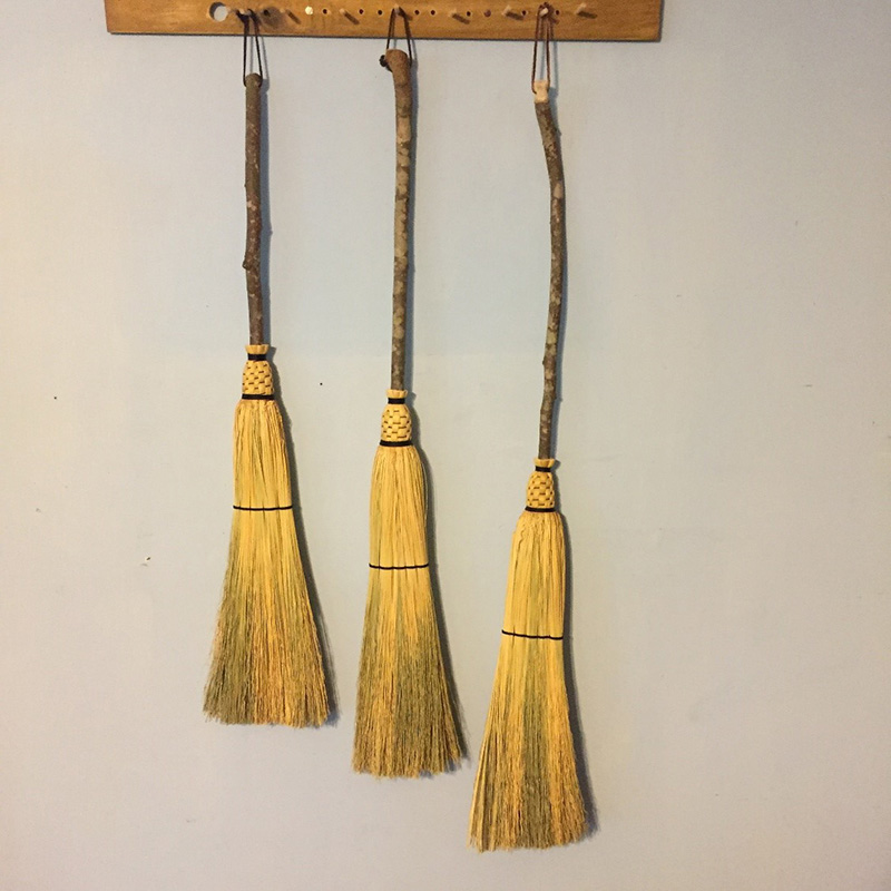 An assortment of rustic flat brooms hanging from wall pegs.