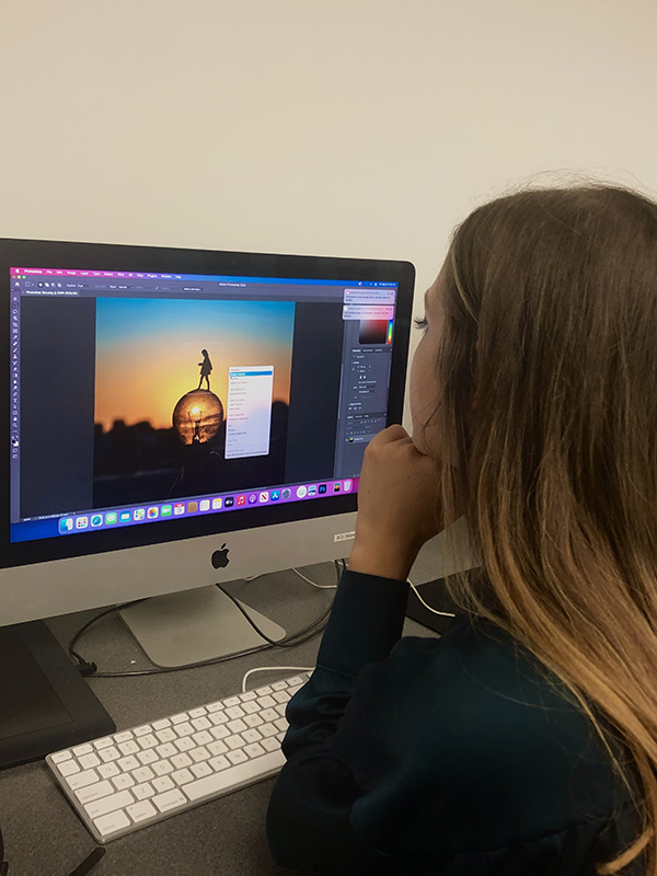 Looking over a woman's shoulder as she works on a surreal image of a sunset in photoshop.