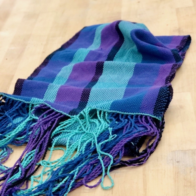 A cool colored scarf with twisted fringe on a wood table.